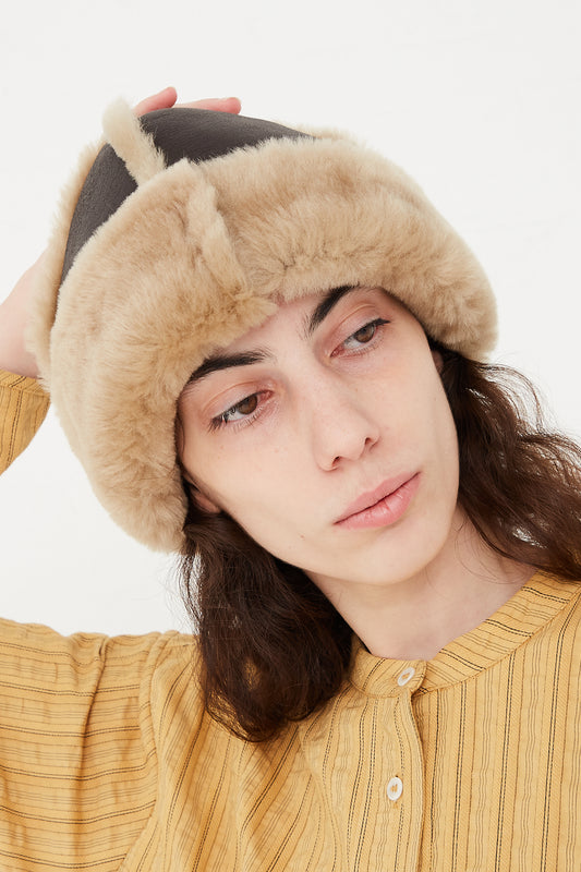 A model wearing a fitted hat in a sheepskin leather.  Head tilted to the side to feature sheepskin. Designed by Cawley - Oroboro Store