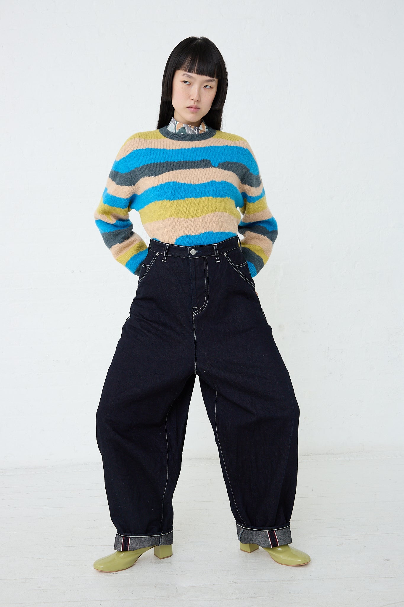A woman wearing a Mina Perhonen relaxed fit striped sweater and Always Balloon Wide Pant in Indigo denim pants. Full legnth and front view. Model's hands in pockets. 
