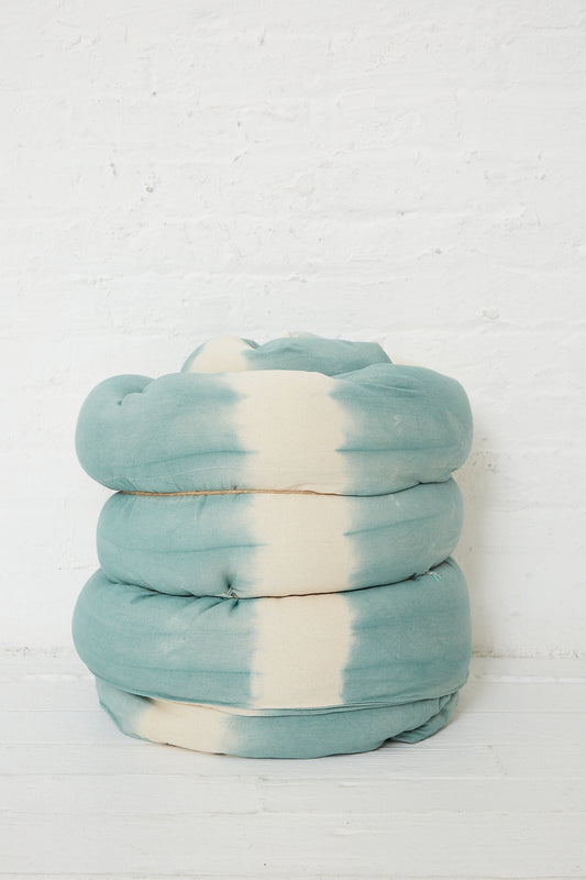 A Tensira Tufted Overlay Mattresses in Celadon Green Tie Dye against a white wall.