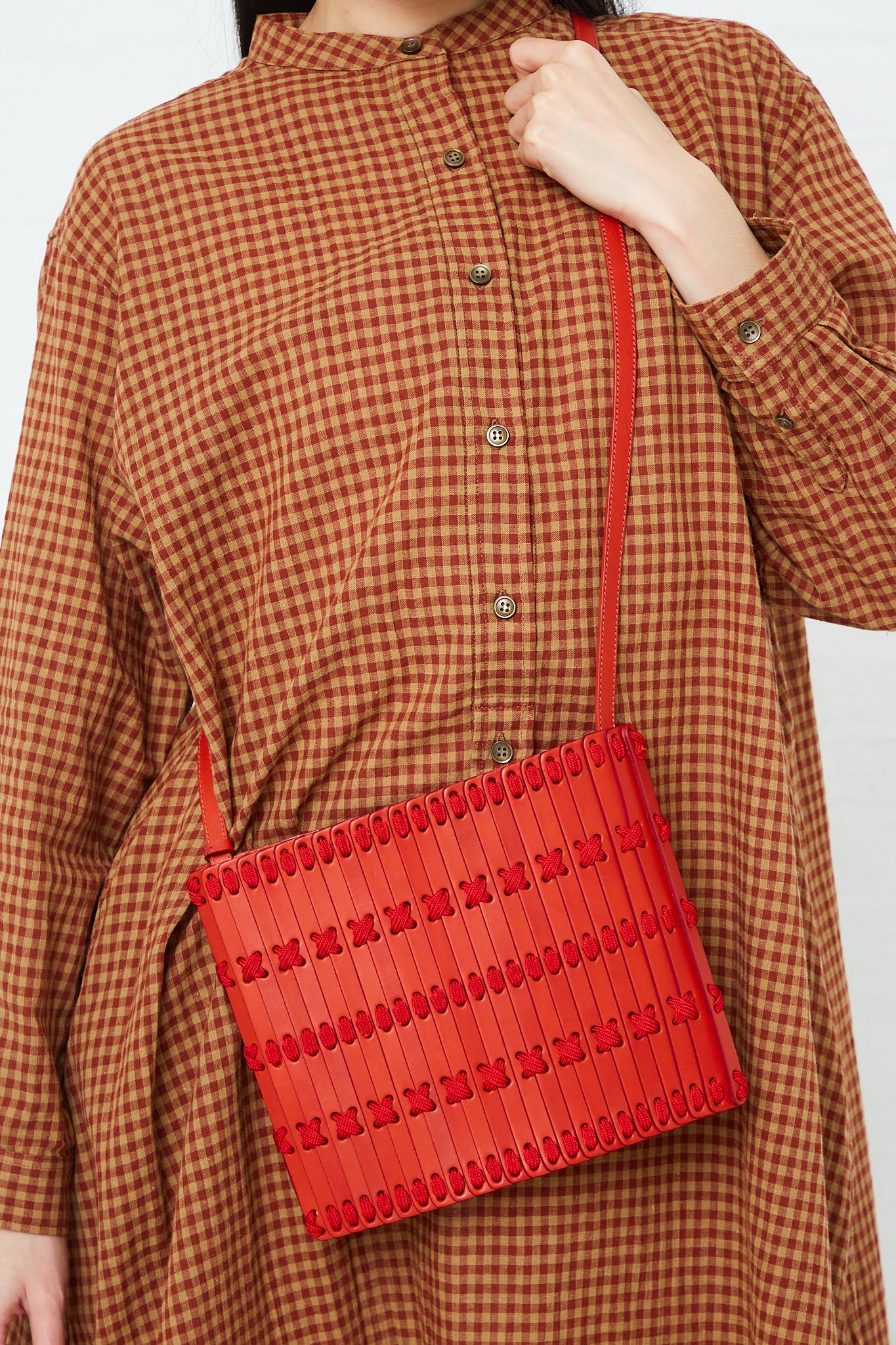A woman in a plaid shirt is holding a handcrafted Hatori Crossbody Bag 46 in Amaranto and Ruby.