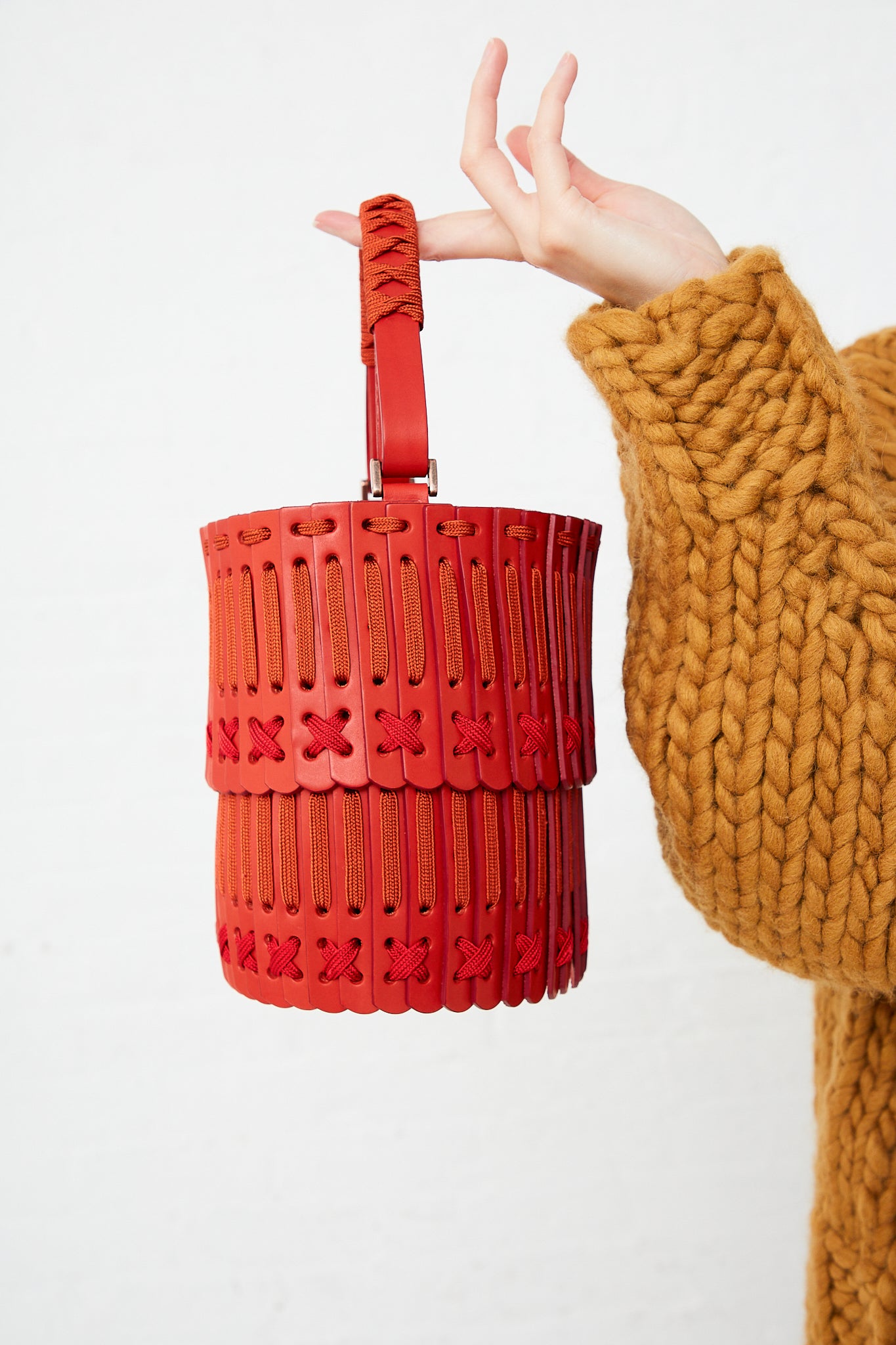 A woman is carrying a Hatori Bucket Bag 80 in Amaranto, Cherry and Tangerine, featuring an adjustable strap and drawstring closure.