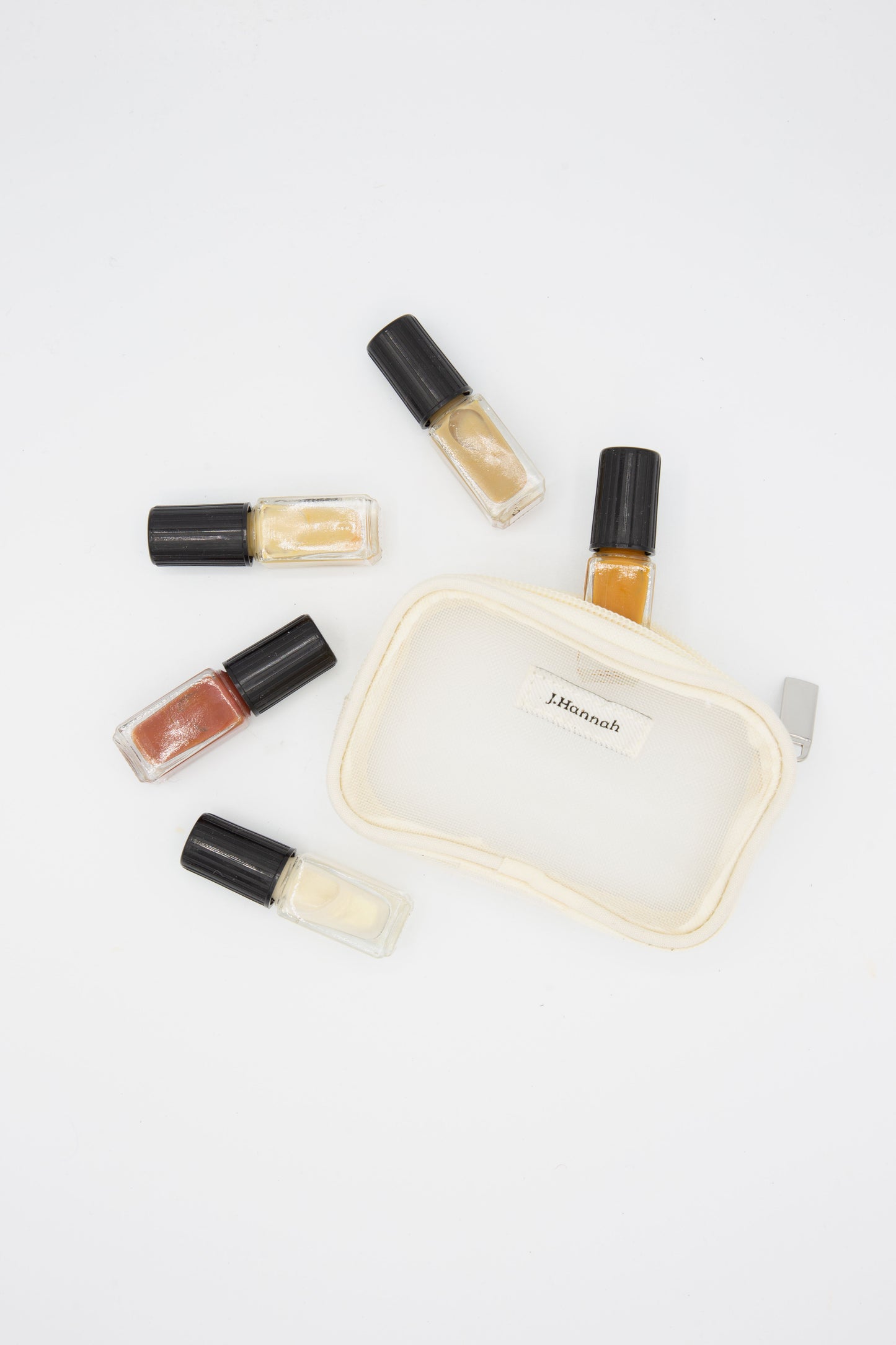A small pouch with a few bottles of J. Hannah Mini Polish Set in Classics, part of a high quality and seven-free nail polish line, on a white surface.