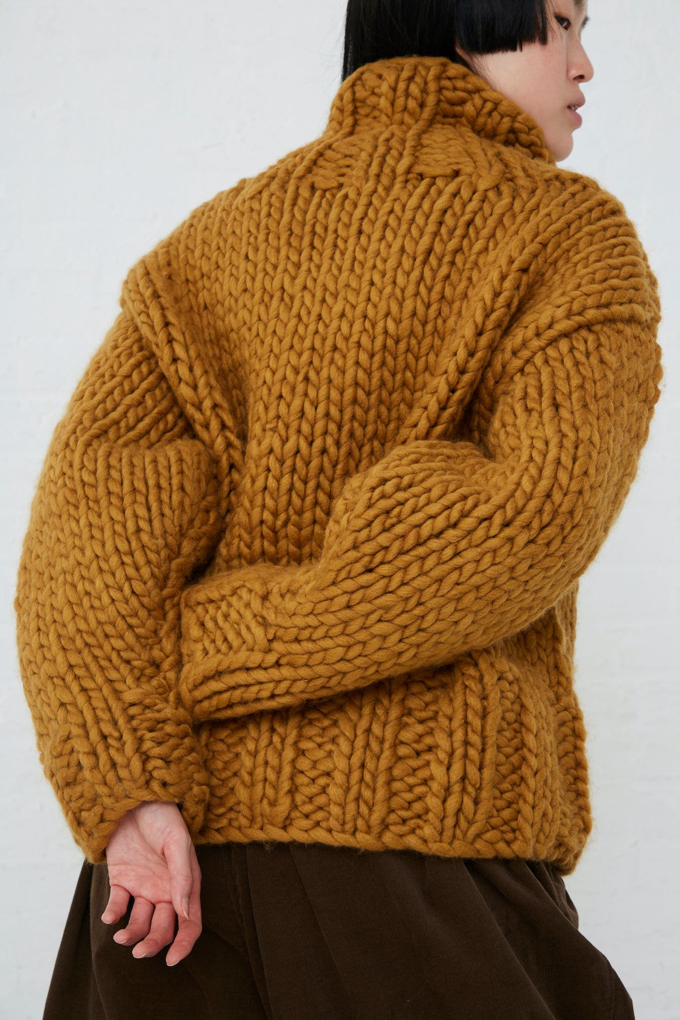 The back of a woman wearing an Ichi Wool Hand-Knit Pullover in Mustard. Arms crossed.