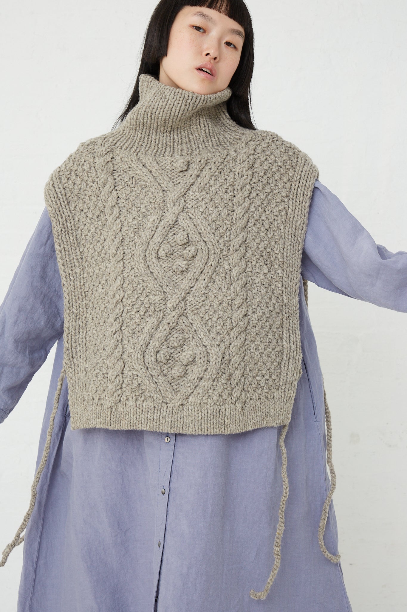 A woman wearing a beige Peruvian Wool Hand Knitted Cable Stitch Vest by nest Robe made from ethically raised sheep wool.