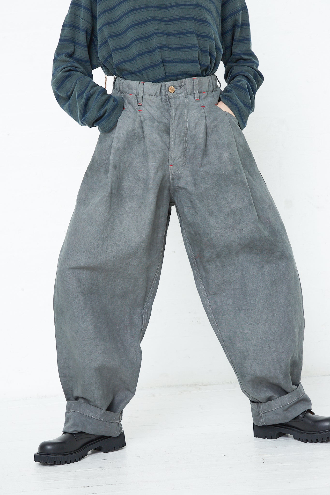 A woman is standing in front of a white wall wearing Dr. Collectors' 9 oz. Cotton and Hemp P40 Z Boys Military Pant in Swiss Army.