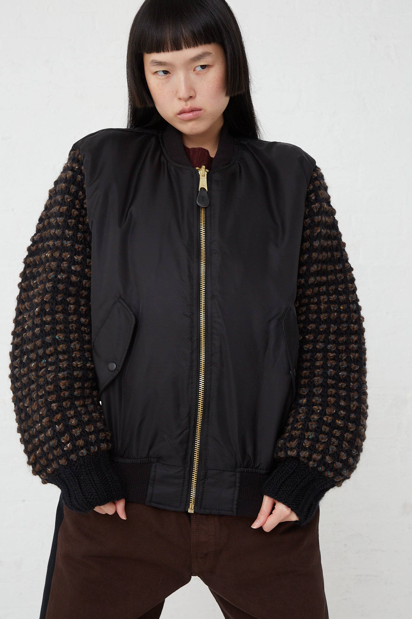 An oversized woman's Bless Sleeve Bomber No. 70 in Black, in a nylon and wool blend, paired with brown pants.