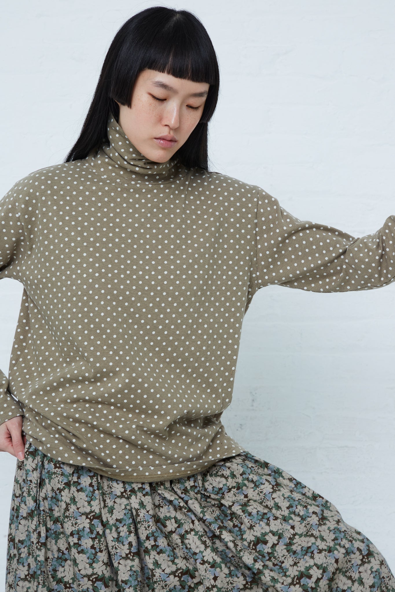 A woman wearing an Ichi Cotton Polka Dot Pullover Turtleneck in Khaki and floral skirt.