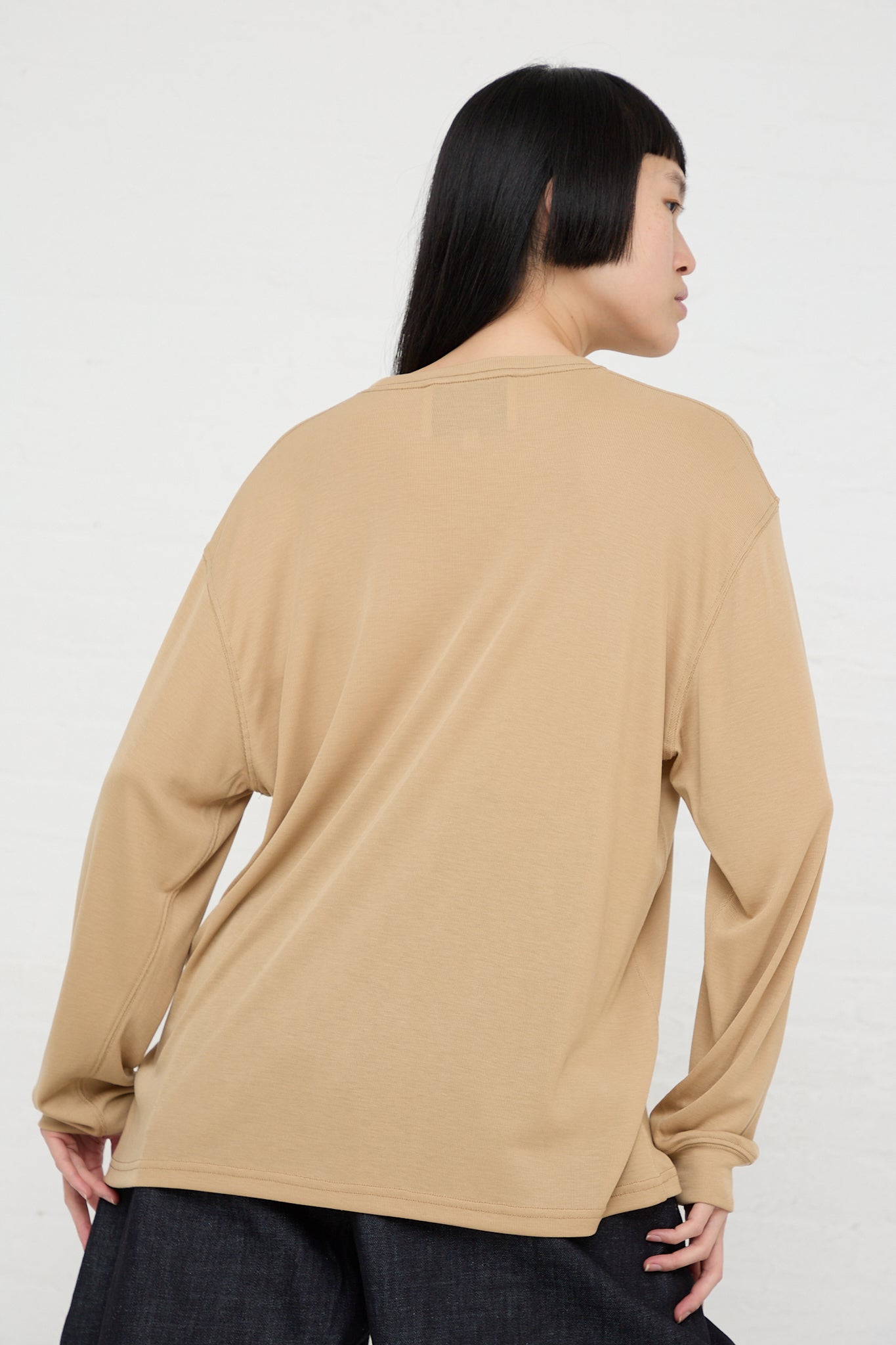 The back view of a woman wearing a Studio Nicholson Simmons Long Sleeve Top in Sand with dropped shoulders.
