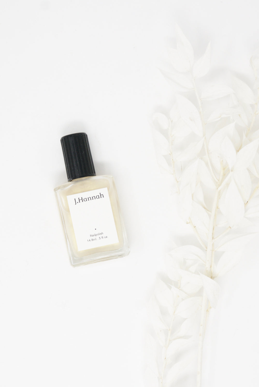 A color-resistant bottle of J Hannah Nail Polish in Akoya sitting on a white surface.