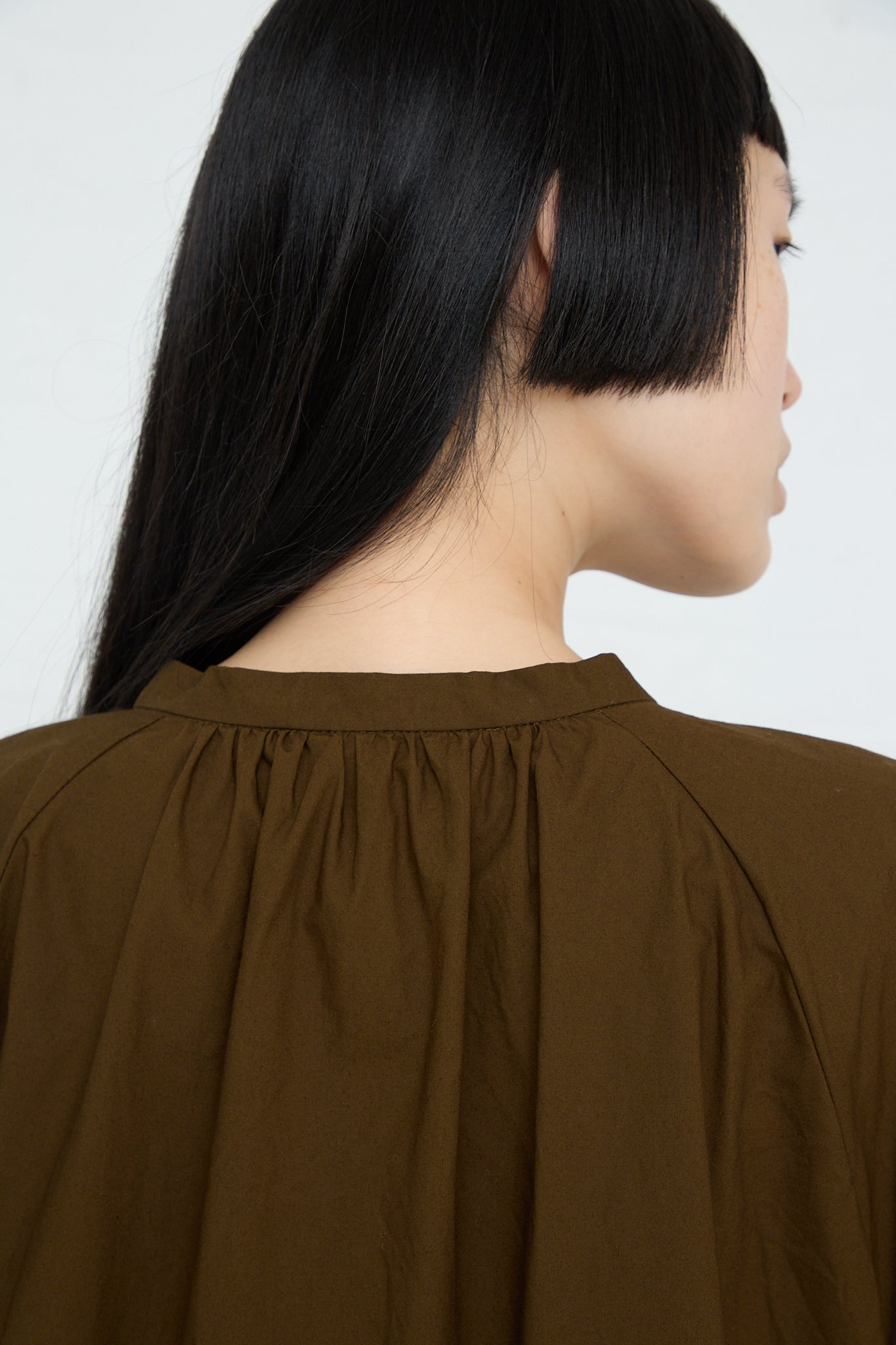 The back view of a woman wearing a Ichi Woven Cotton Shirt in Seal Brown wide band collar top.