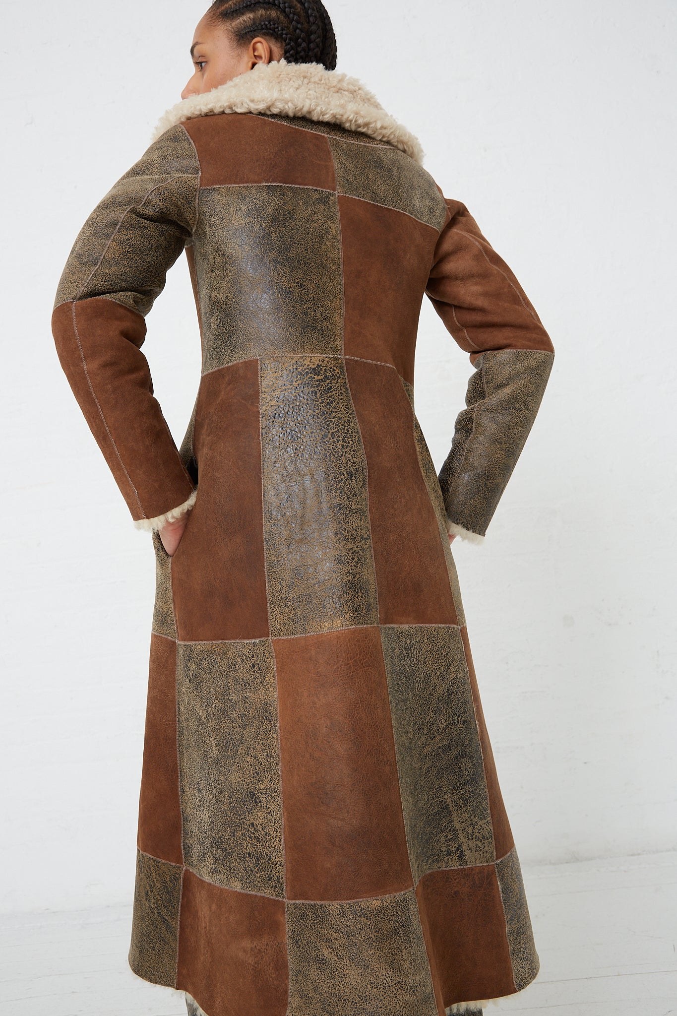 The back view of a woman wearing a Milena Silvano Sheepskin Albizia Coat in Tonal. Full length.