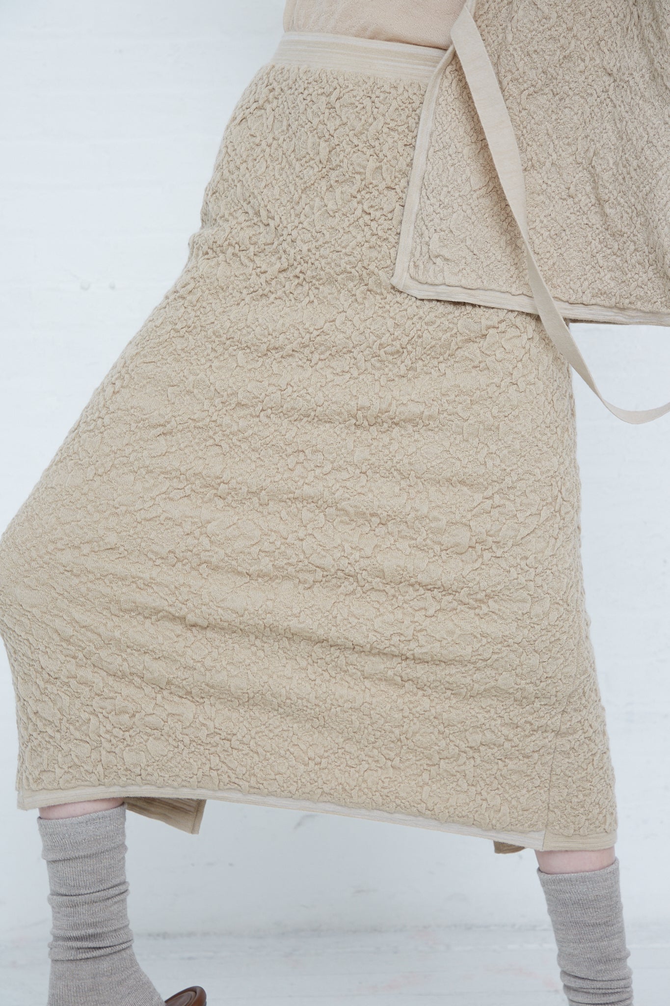 A woman wearing a Lauren Manoogian Baby Alpaca Gauze Skirt in Antique. Up close view of skirt details. Model is wearing the skirt with a matching cardigan.