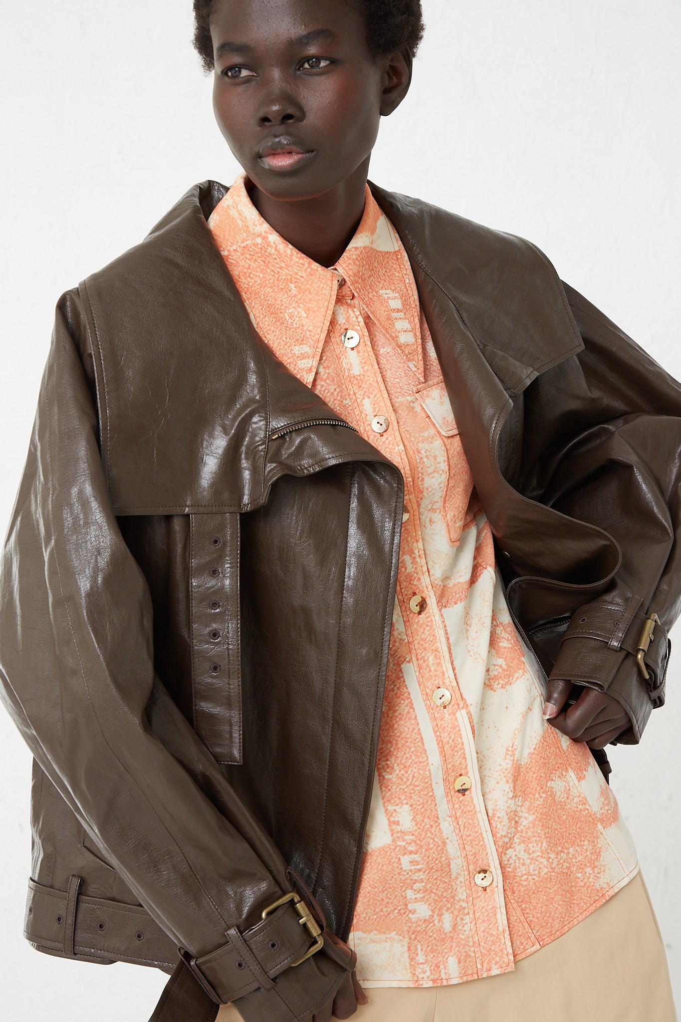 A model wearing a Rejina Pyo Faux Leather Juno Jacket in Dark Brown and orange shirt.