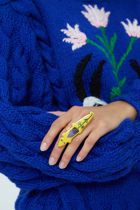 A woman wearing a blue sweater and Sofio Gongli Ring in Yellow Alligator with Flower.