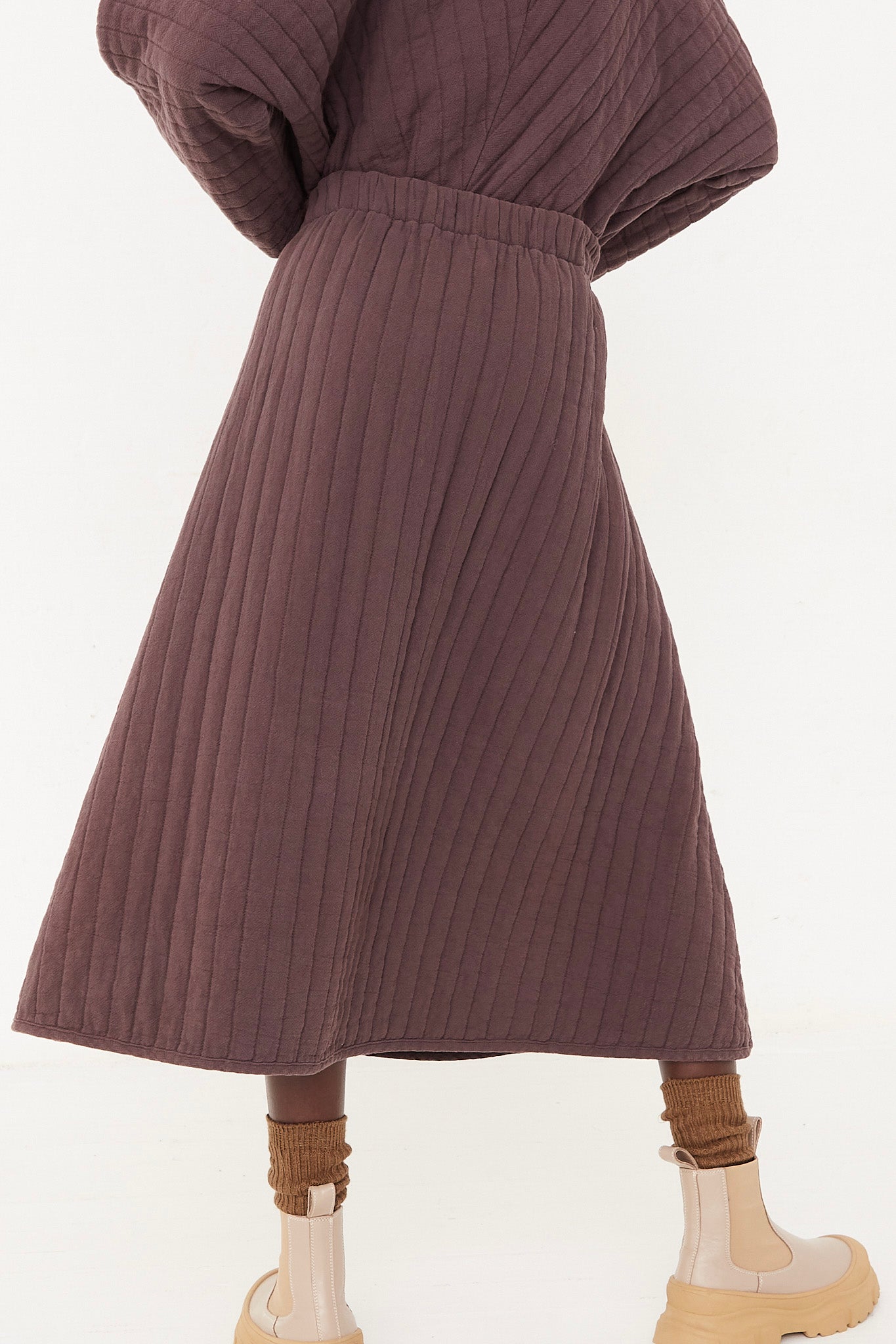 The back of a woman wearing a Black Crane Quilted Skirt in Plum with an elasticated waist.