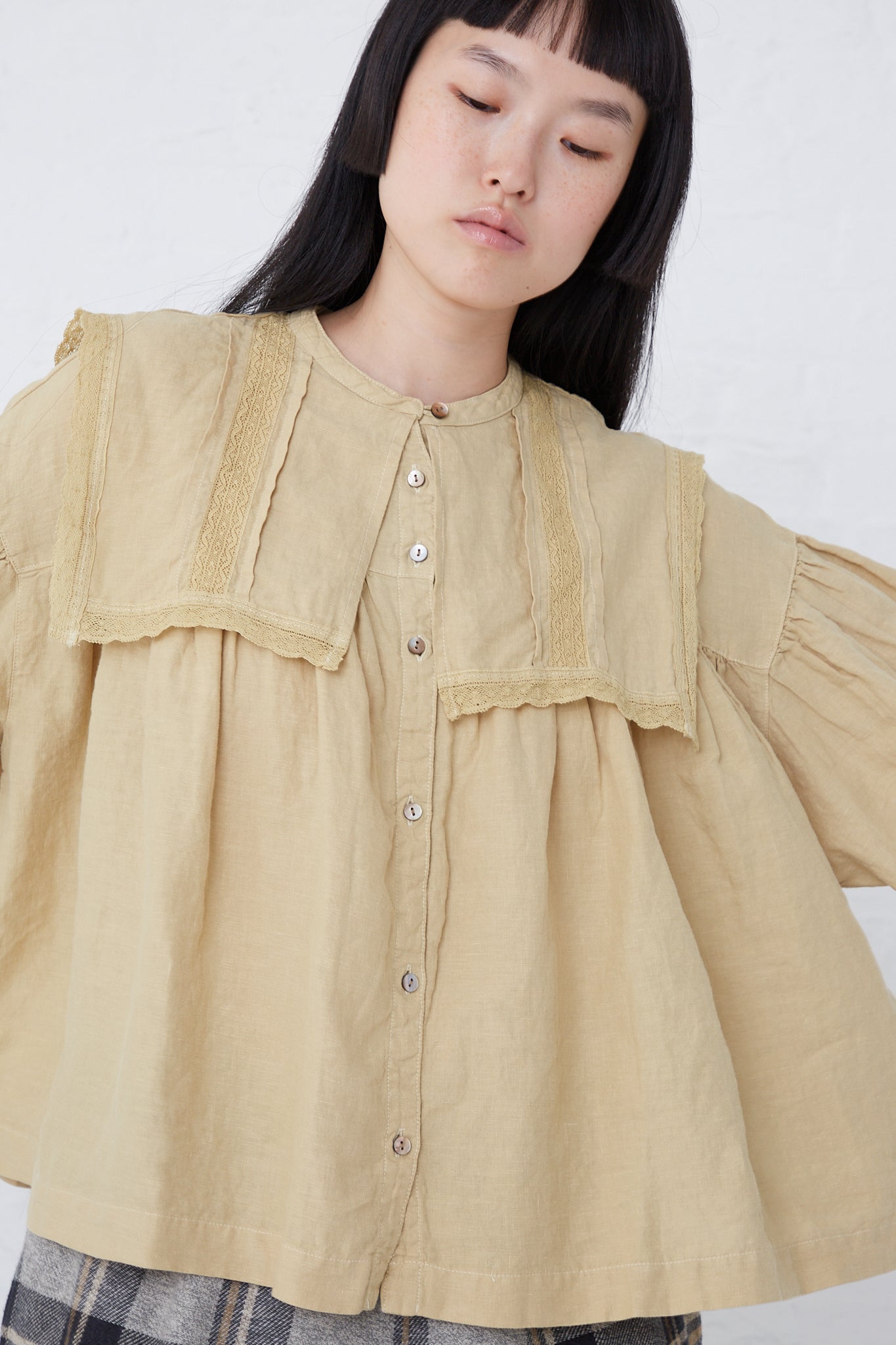 The model is wearing a Natural Dyed Linen Lace Blouse in Yellow from nest Robe with ruffles and a sailor collar.