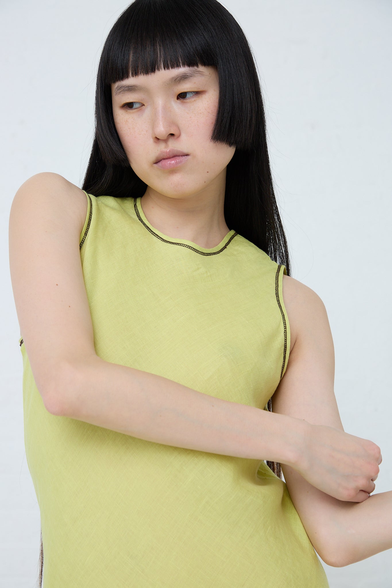 A woman in a Baserange Linen Dydine Tank Dress in Lime with black hair. Up close and front view.
