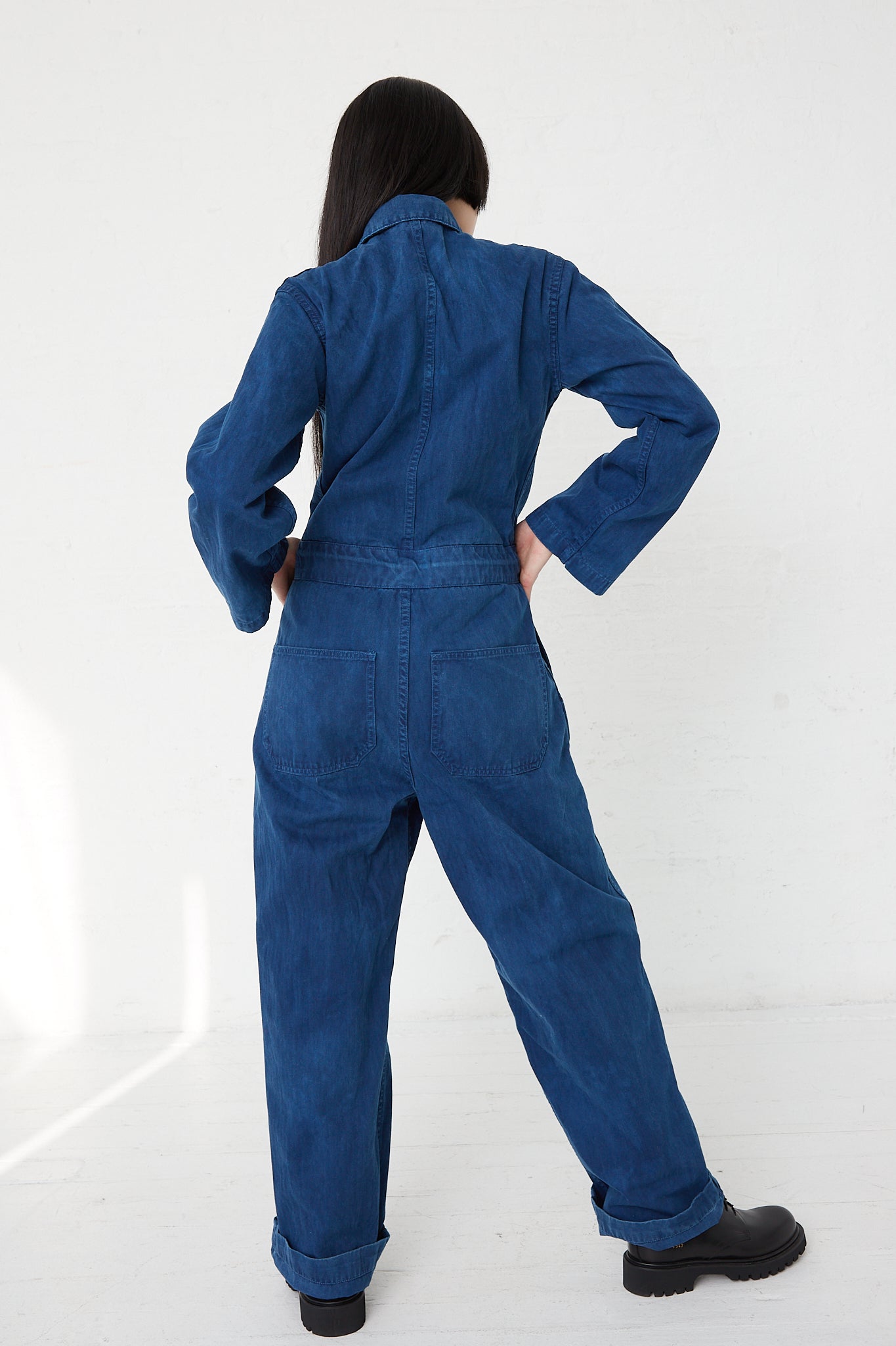 A woman wearing an As Ever front zip jumpsuit in Indigo. Back view.