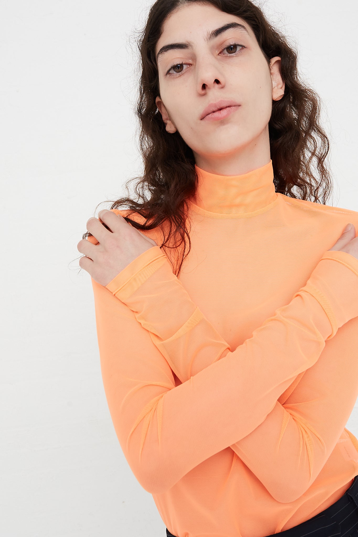 A model wearing the Long Sleeve Mesh Mockneck in Fluoro Orange designed by Nomia brand.