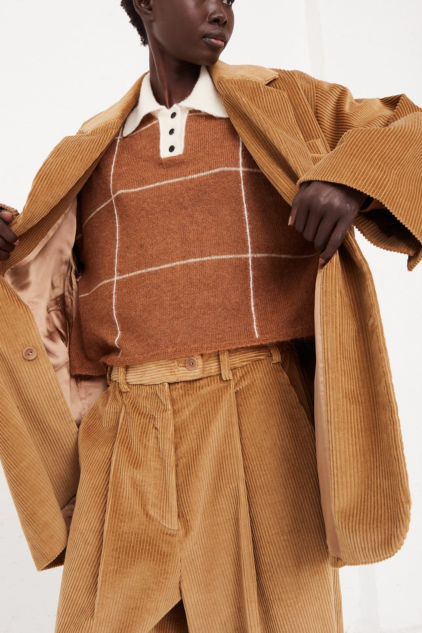 A model wearing a button blazer in a cotton corduroy featuring a notched collar, two flap pockets in front, and back vent. Blazer being held open by model highlighting lining, knit and pants. Oversized fit. Designed by Cordera - Oroboro Store