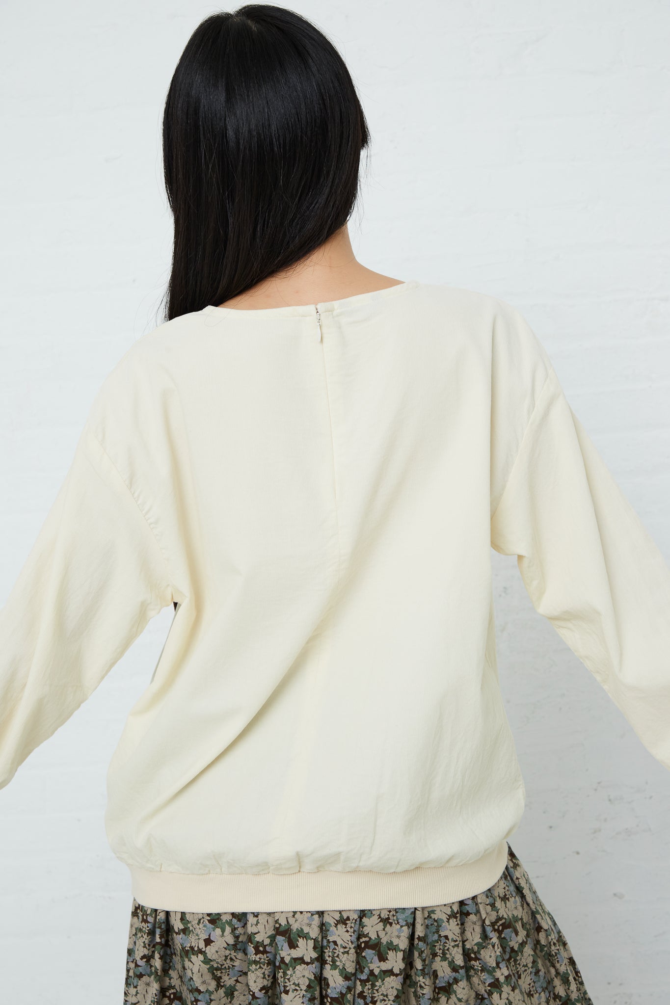 The back of a woman wearing an Ichi Cotton Pullover in Ivory and floral skirt.