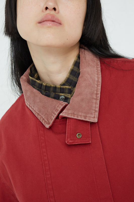 An oversized fit Chimala Canvas Riding Coat in Burgundy, made of cotton canvas, worn by a woman in a red coat and a plaid shirt.