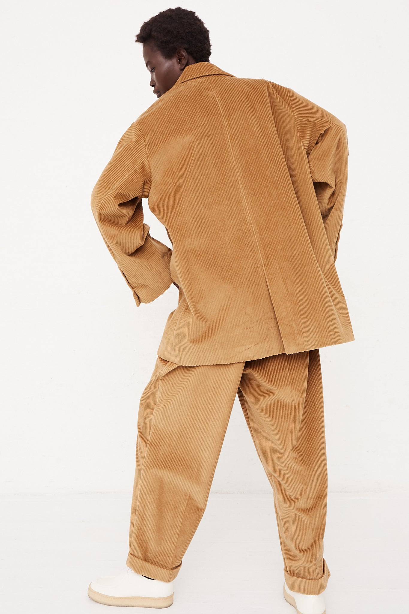 A model wearing a button blazer in a cotton corduroy featuring a notched collar, two flap pockets in front, and back vent. Back full view of blazer. Oversized fit. Designed by Cordera - Oroboro Store