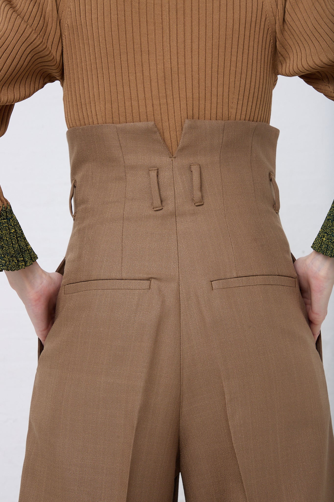 The back view of a woman wearing TOGA PULLA brown high waist trousers made of a woven rayon blend fabric.