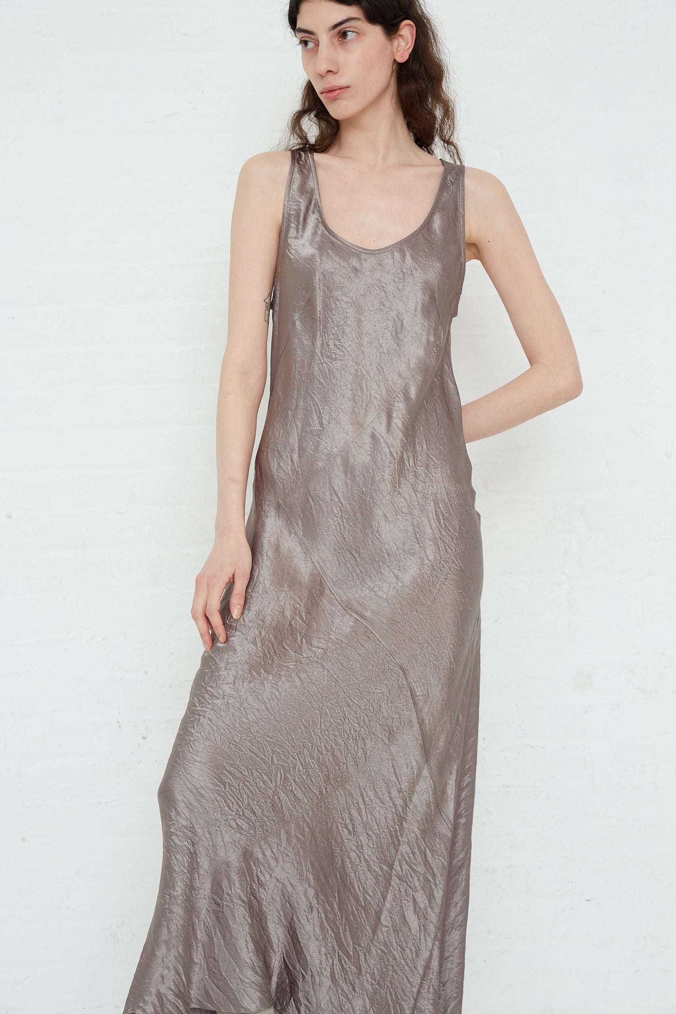 A woman wearing a long sleeveless Luster Bias Dress in Laurel by Lauren Manoogian, made of silver metallic maxi dress with a soft sheen rayon fabric.