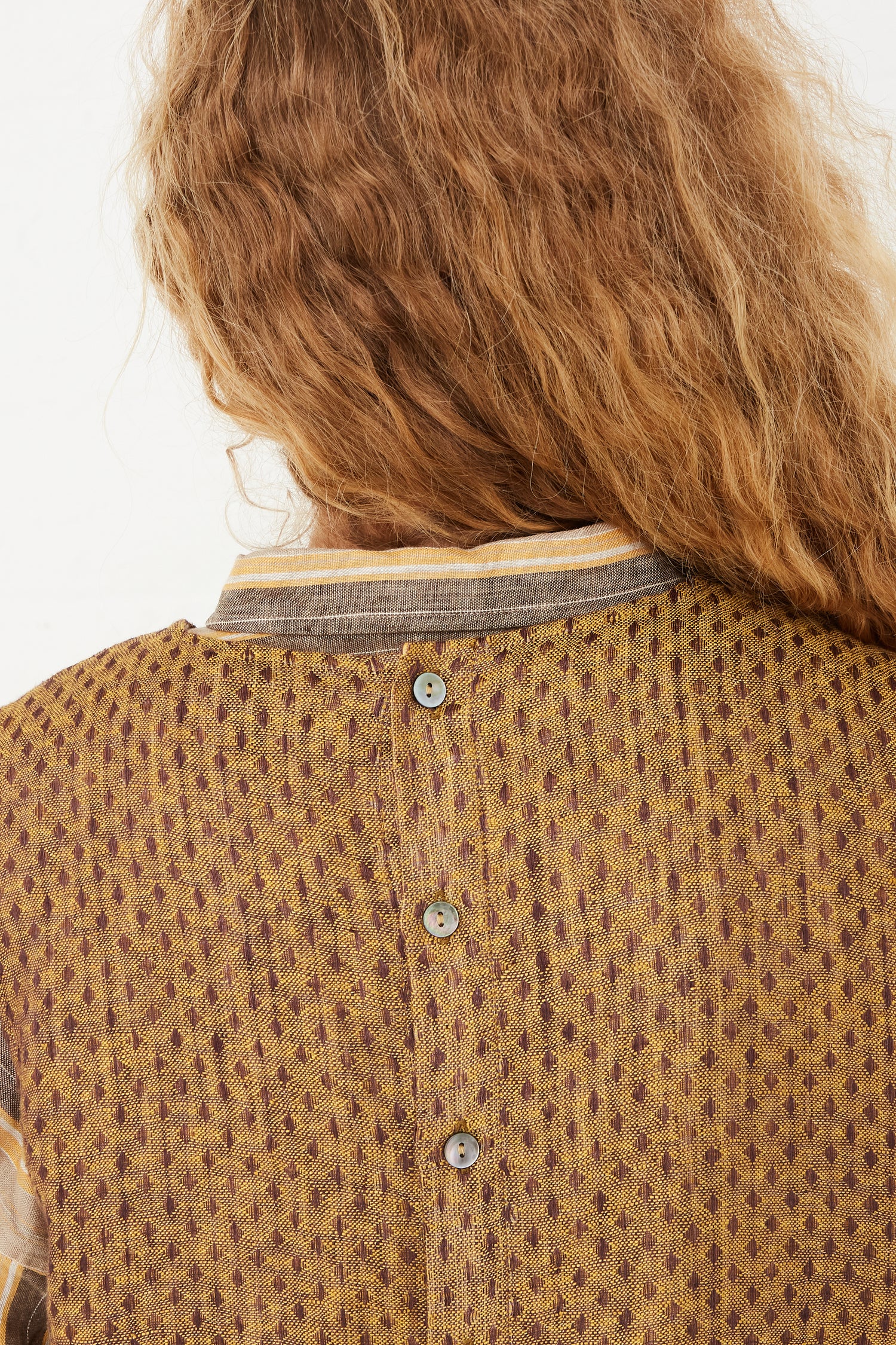 The back view of a model wearing an Ichi Antiquités Linen Dobby Pullover in Camel. Highlighting back button closure.