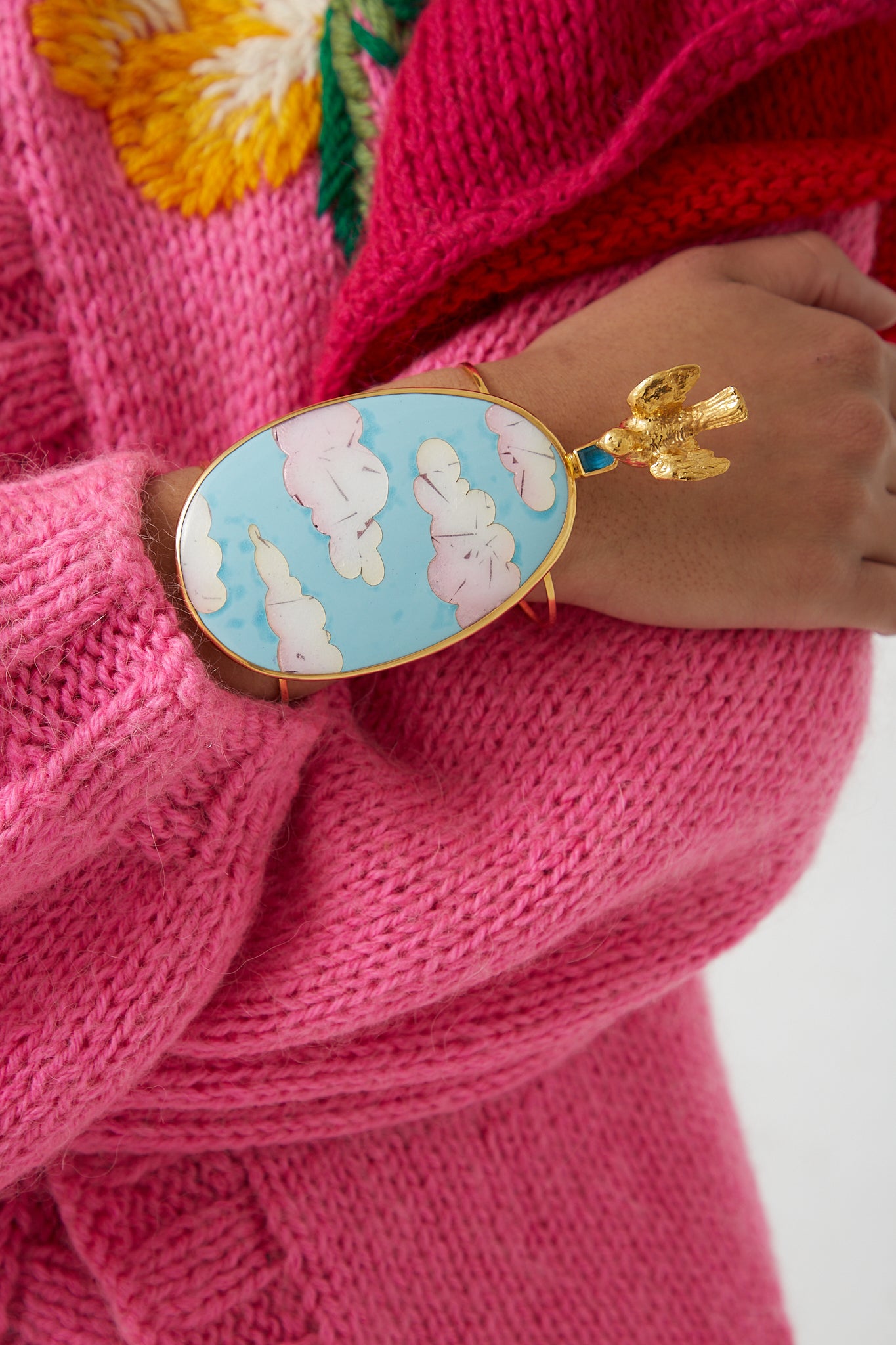 A woman wearing a pink sweater with a blue and white cuff accessorized with a Sofio Gongli Bracelet in Clouds with Bird.