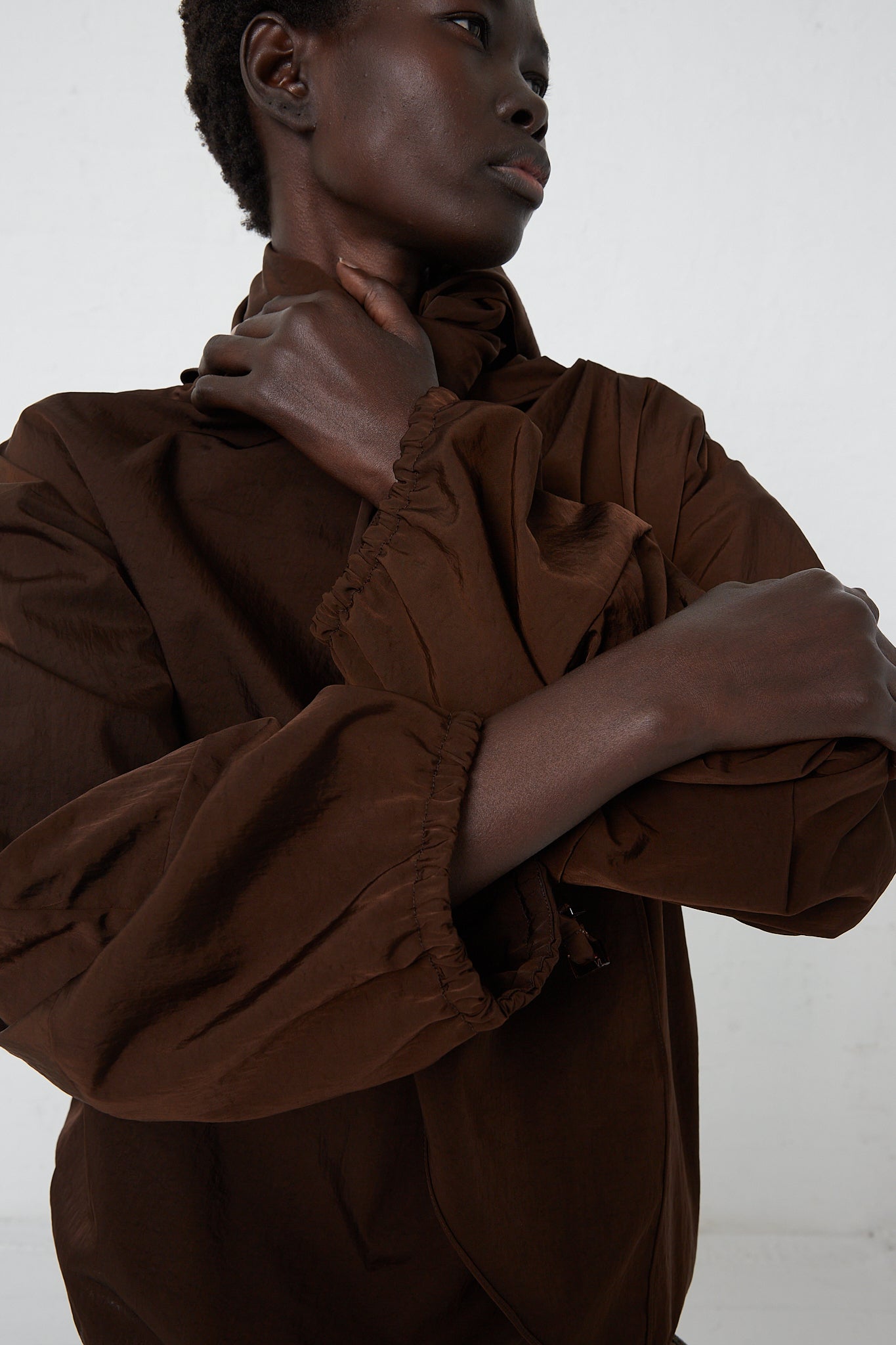 A woman in a brown shirt posing in front of a white background wearing the Veronique Leroy Zipped on Sleeve Rain Blouse in Choco.