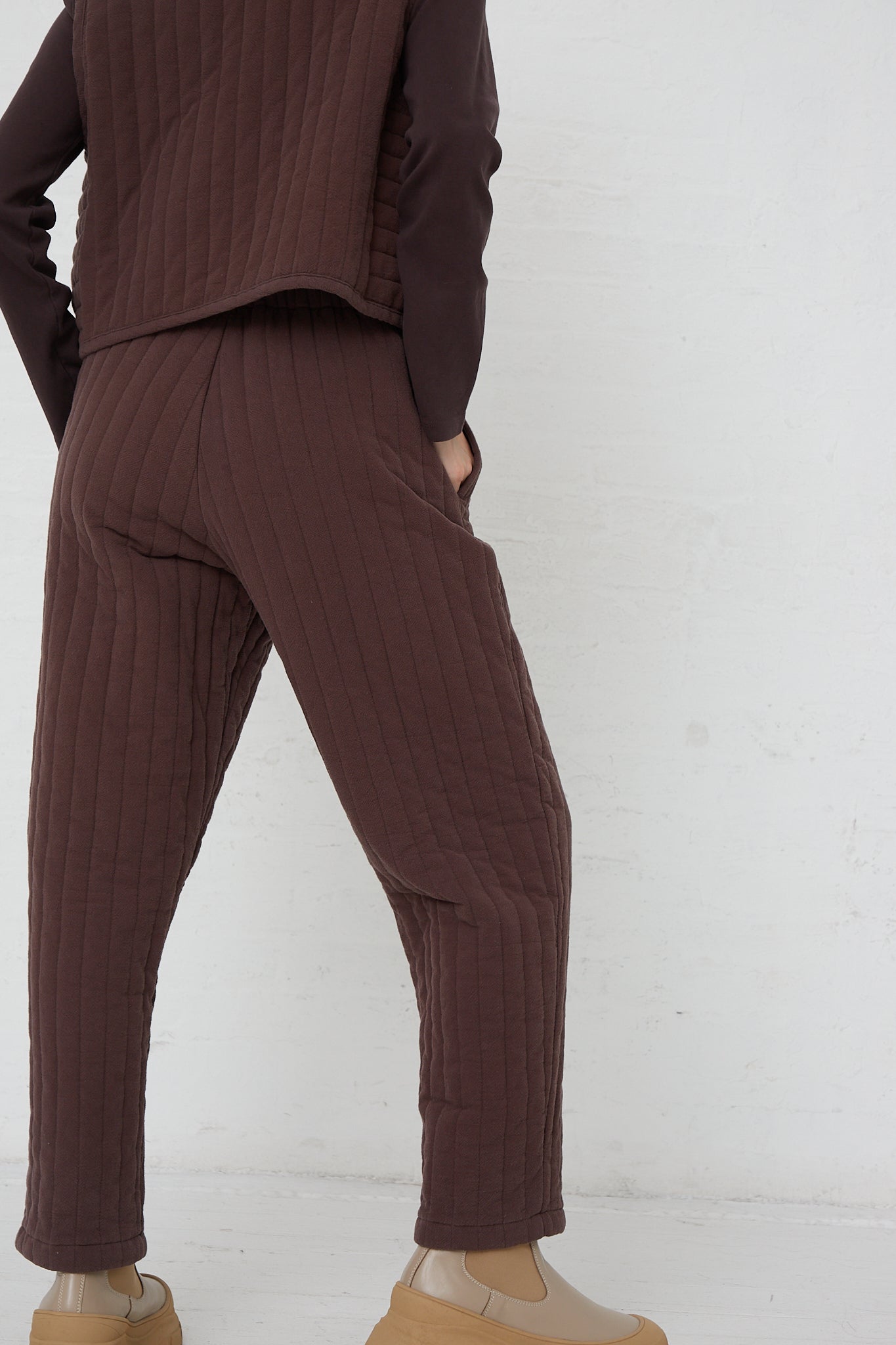 The back of a woman wearing Black Crane's Quilted Easy Pants in Plum, in a relaxed fit.