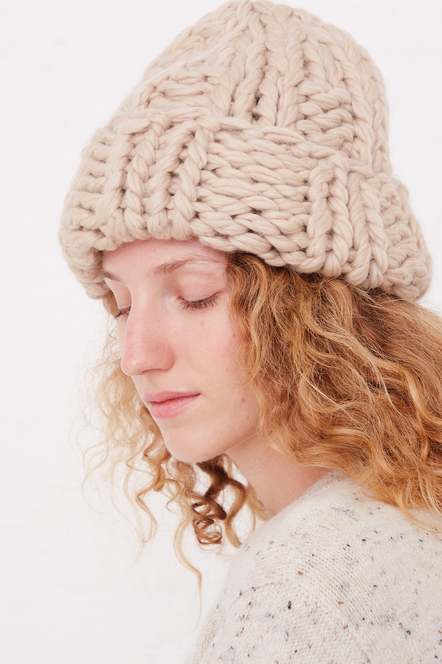 A woman with curly hair wearing an oversized Lauren Manoogian Handknit Chunky Rib Hat in Antique.