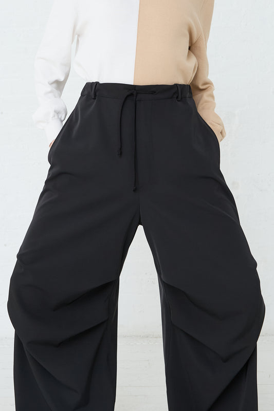 A woman wearing MM6 black wide leg twill stretch pants and a white oversize shirt. Front view and up close.