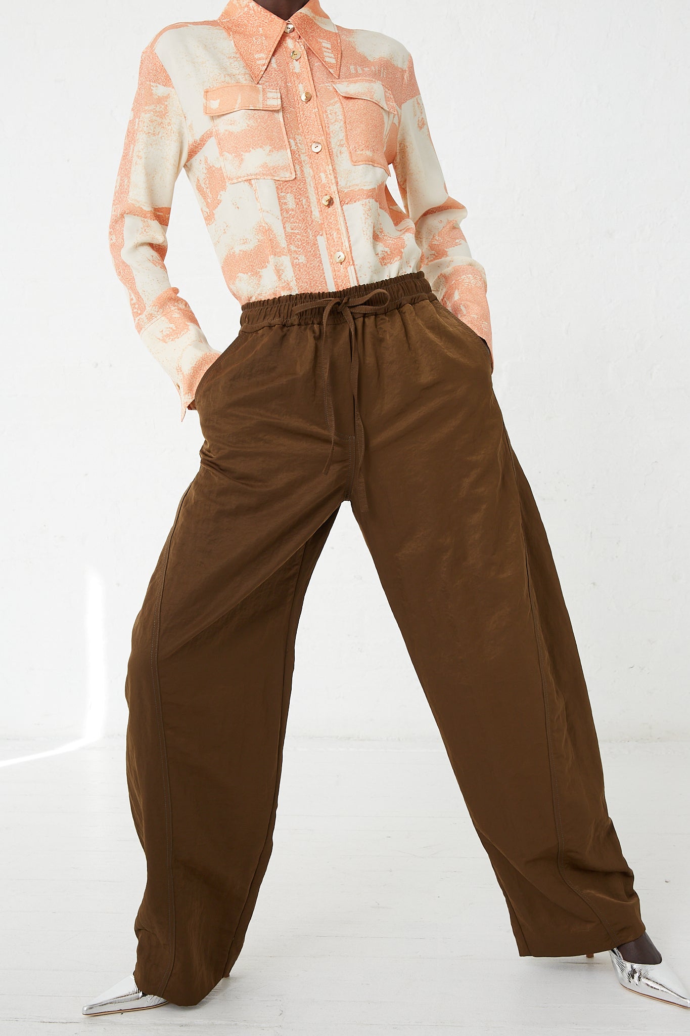 A woman wearing Rejina Pyo's Nylon Una Trousers in Brown with an elasticated waist.