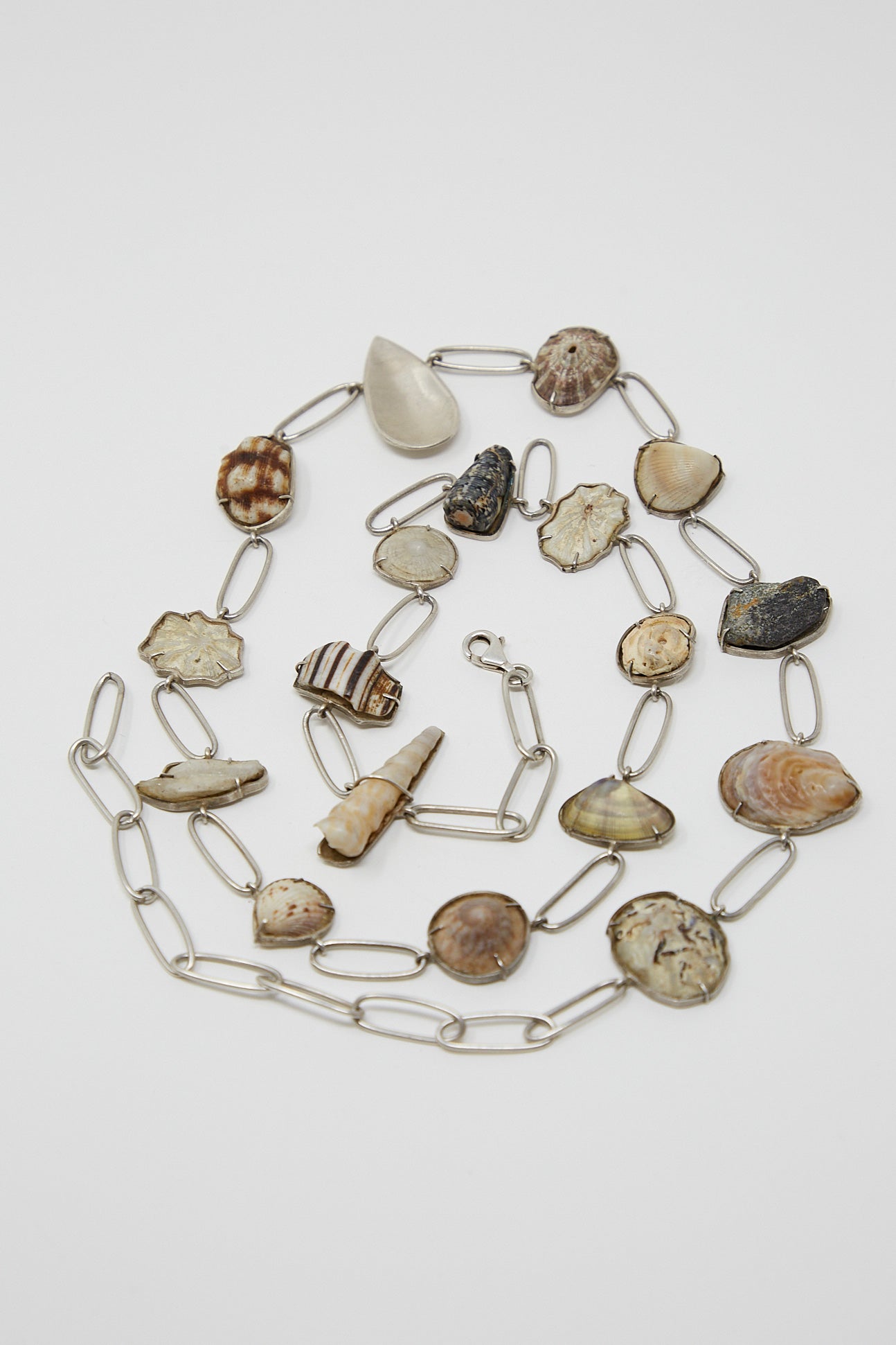 A unique collection of La Mar sterling silver shell belt 013 and stones on a white surface.