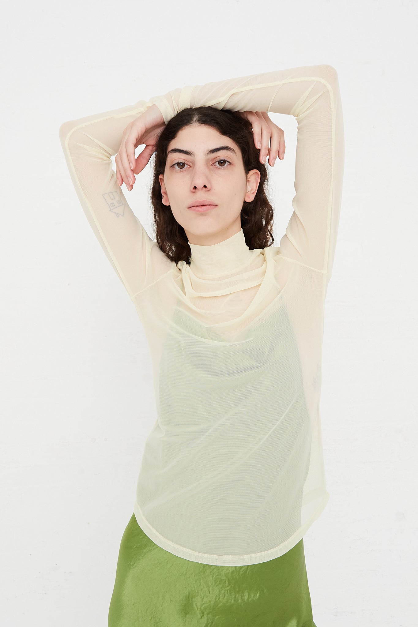 A model wearing a green skirt and a cream turtle neck top, available at Oroboro Store.