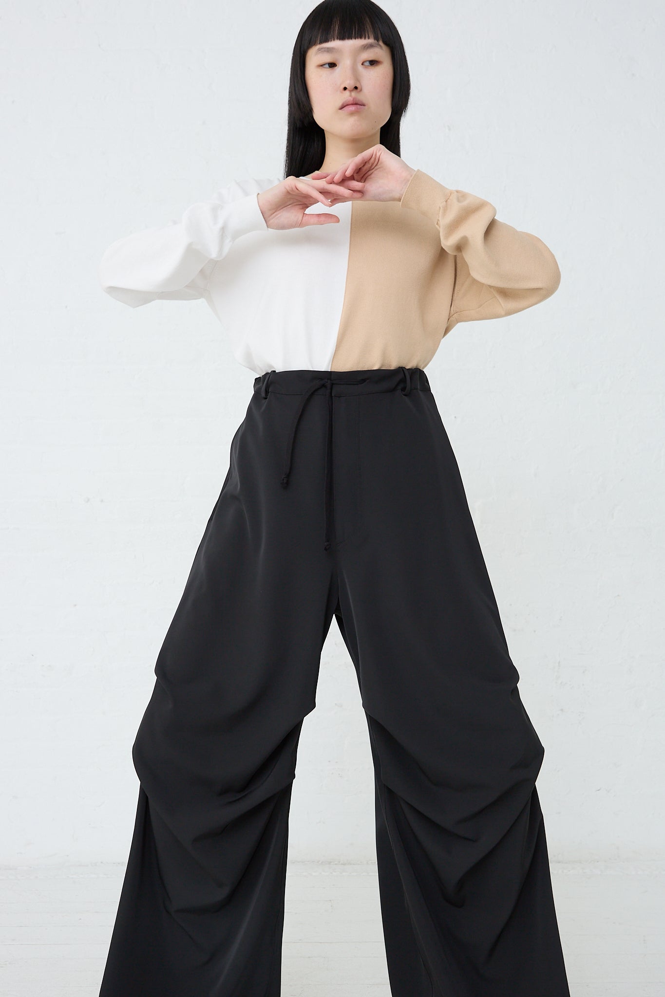 A model wearing MM6's Pant in Black, an oversized silhouette black wide leg pants with a drawstring waist, and a beige twill stretch top. Front view and full length.