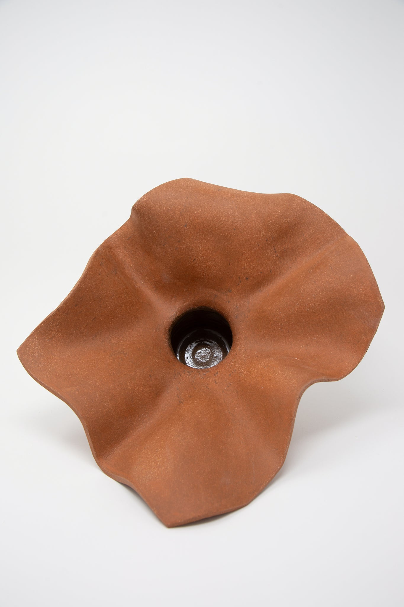 Introducing the Ruffle Pedestal in Terracotta by Lost Quarry, a uniquely shaped, hand-built clay sculpture featuring a central hollow cavity and wavy edges, beautifully captured against a plain white background.