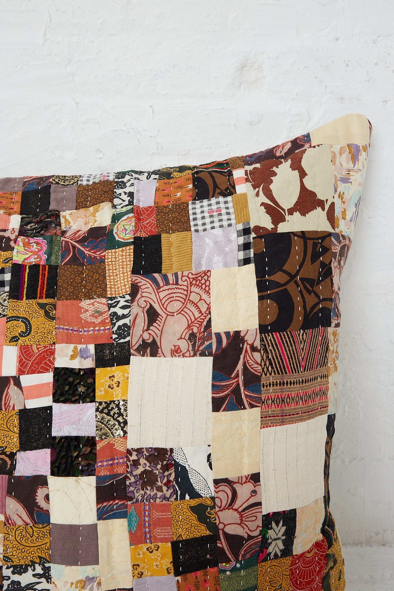 An antique found cloth transformed into a Counterpane Patchwork Pillow in Brown Multi I with a patchwork pattern.