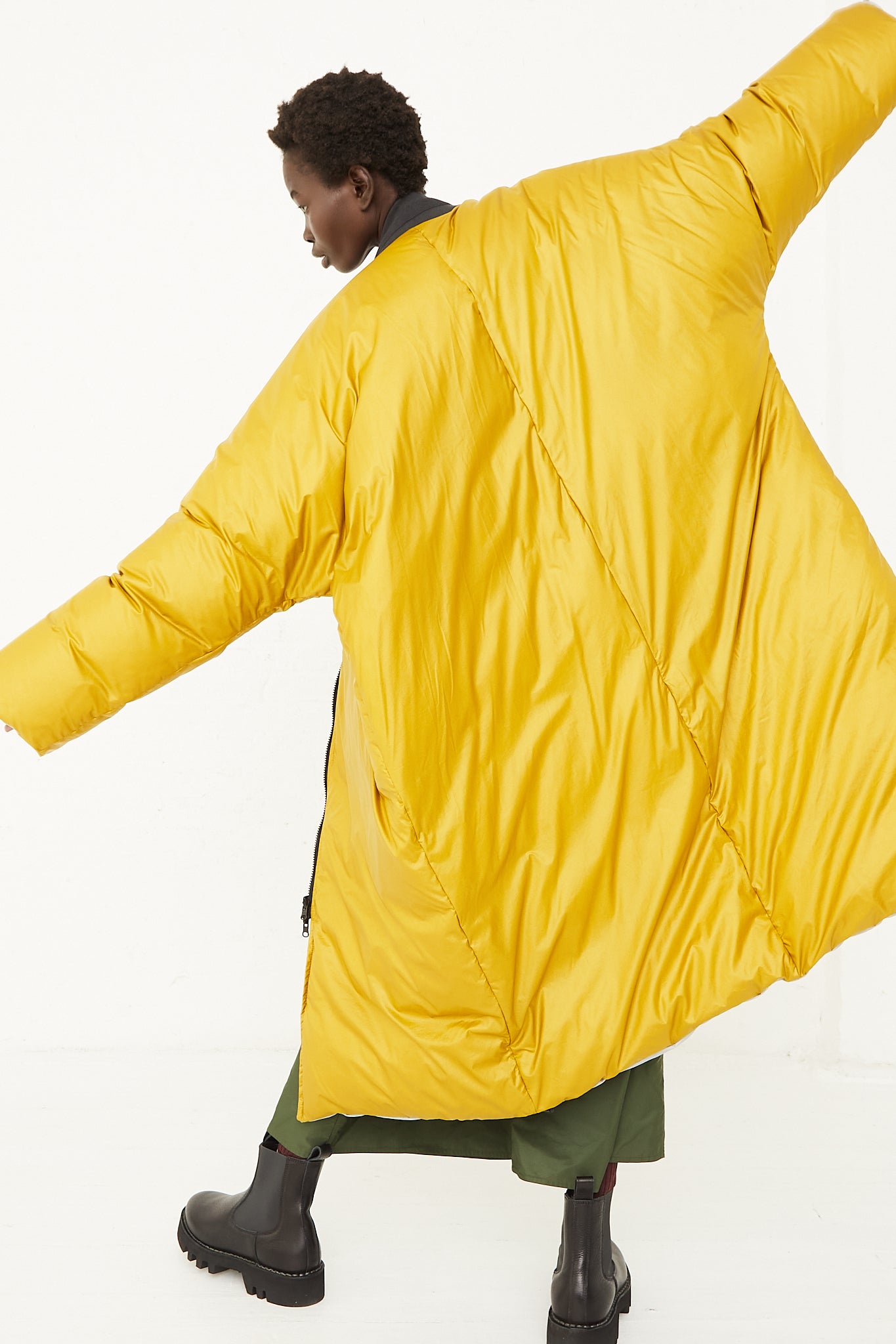 A model wearing an oversized down jacket in a water repellent nylon. Features a bomber collar, zip closure, adjustable ties at hem and a reversible fit. Full length and back view. Featuring the gold option. Designed by Sofie D'Hoore - Oroboro Store