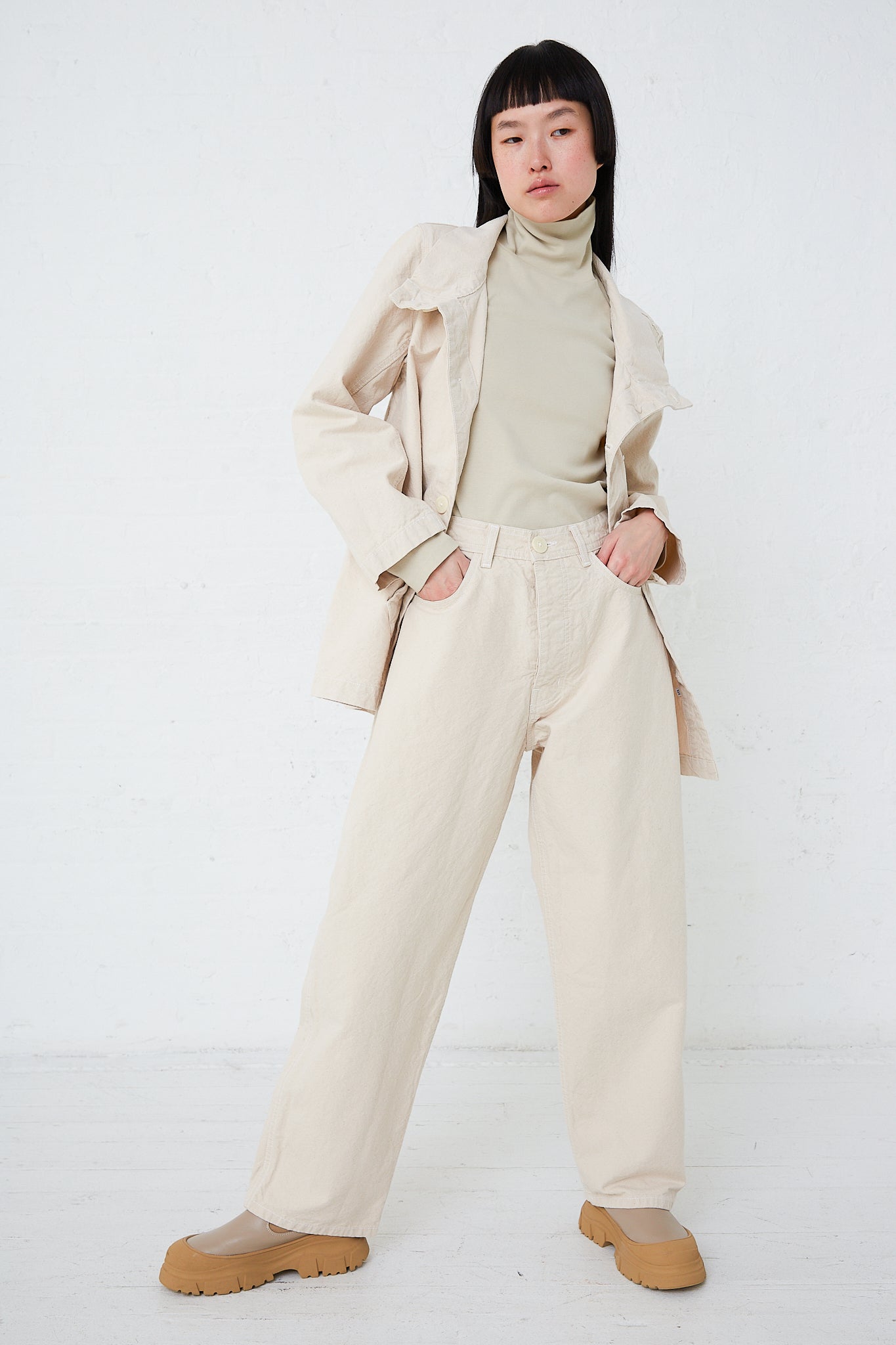 A woman in Jesse Kamm's Organic Canvas California Wide pants in Natural, paired with a turtle neck top.