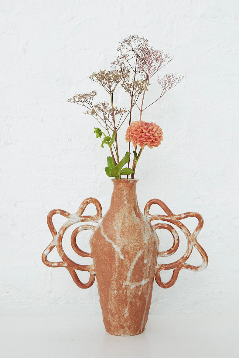 A Tall Amphora Bloom Vase with handmade flowers in it, sitting on a white wall. (Brand: Clandestine)