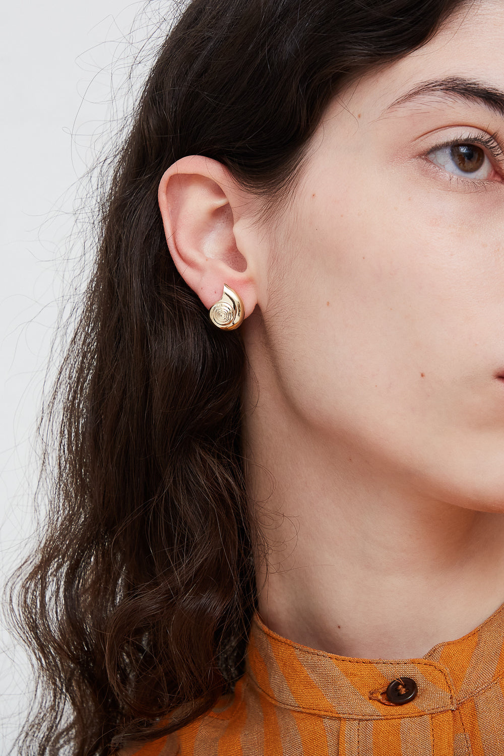 A woman wearing handmade Kathryn Bentley Large Nautilus shell earrings with gold stud earrings.