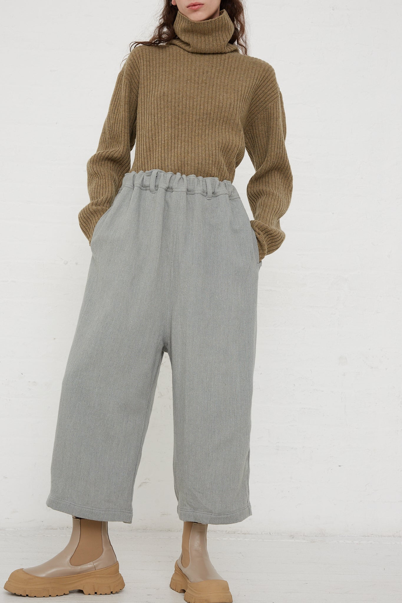 The model is wearing a Merino Wool Orihimedaki Pant in Blue and grey wide leg pants with an elasticated waist.