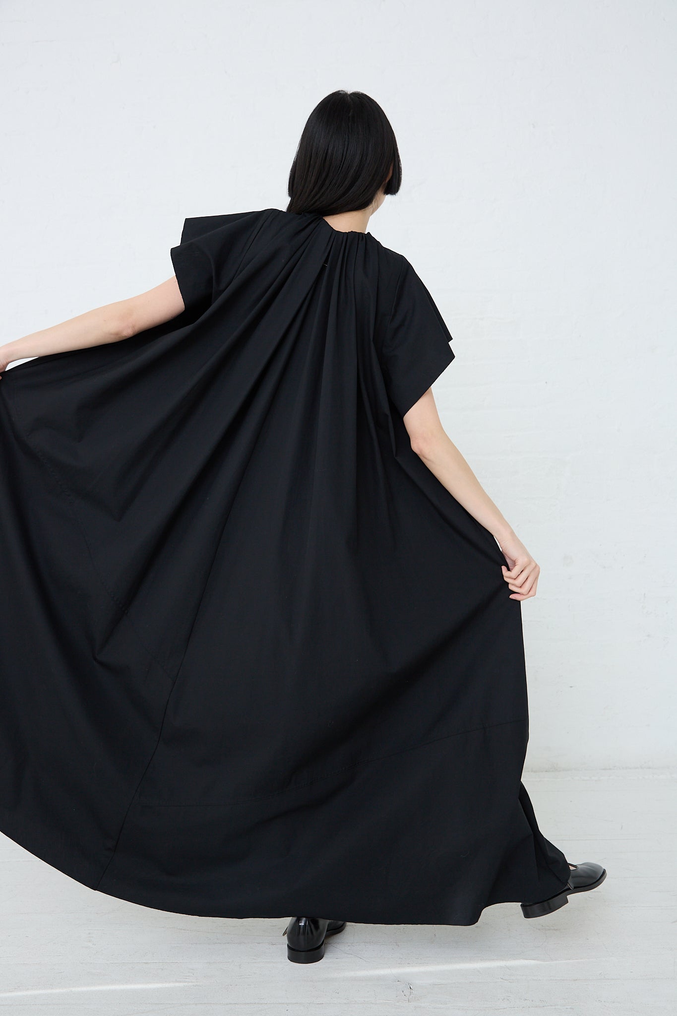 A woman wearing a MM6 black maxi dress with an oversized fit. Back view and full length.