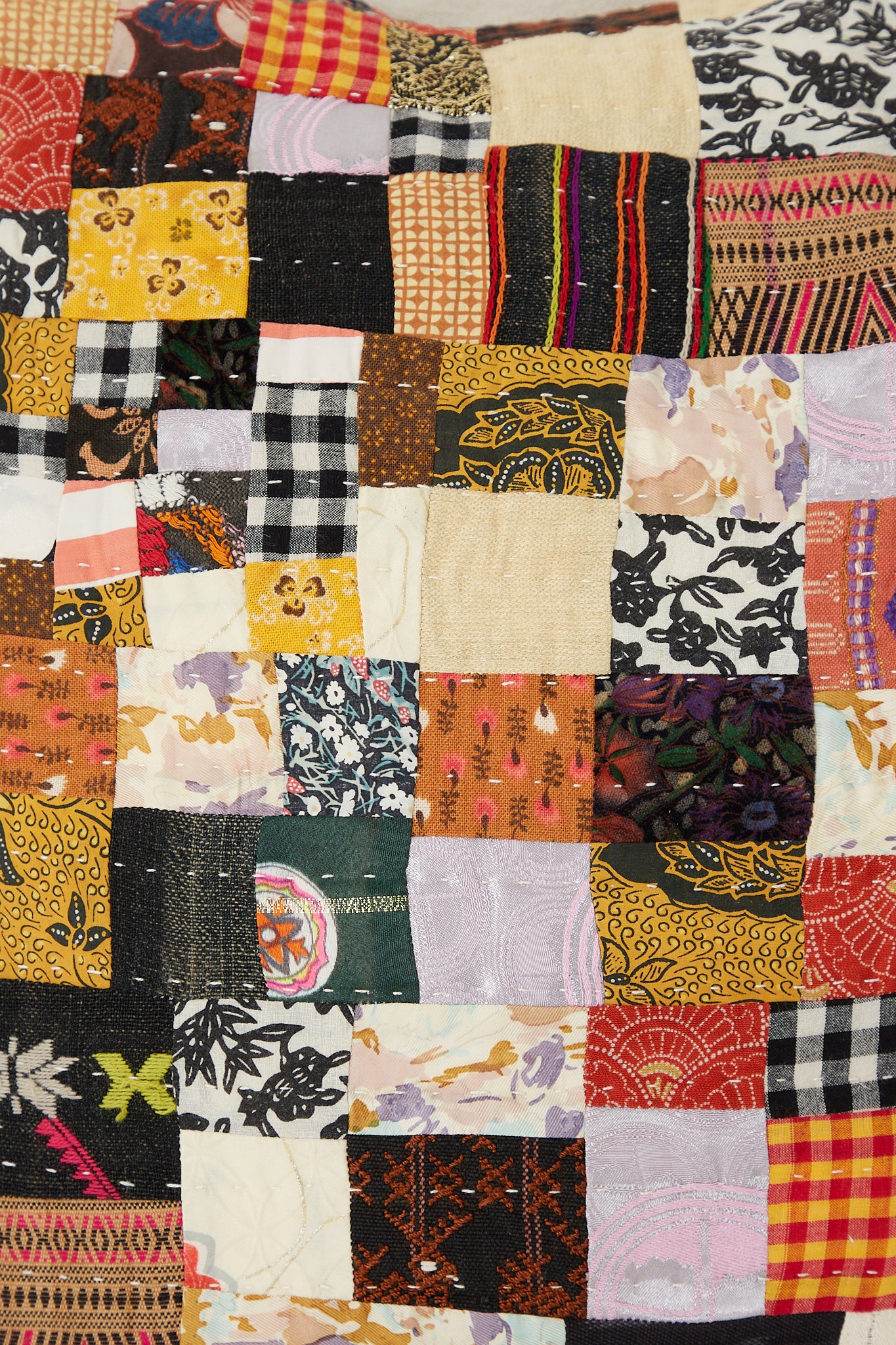 A close up of an antique found cloth, featuring a Counterpane Patchwork Pillows in Brown Multi II in a freehand quilting style.