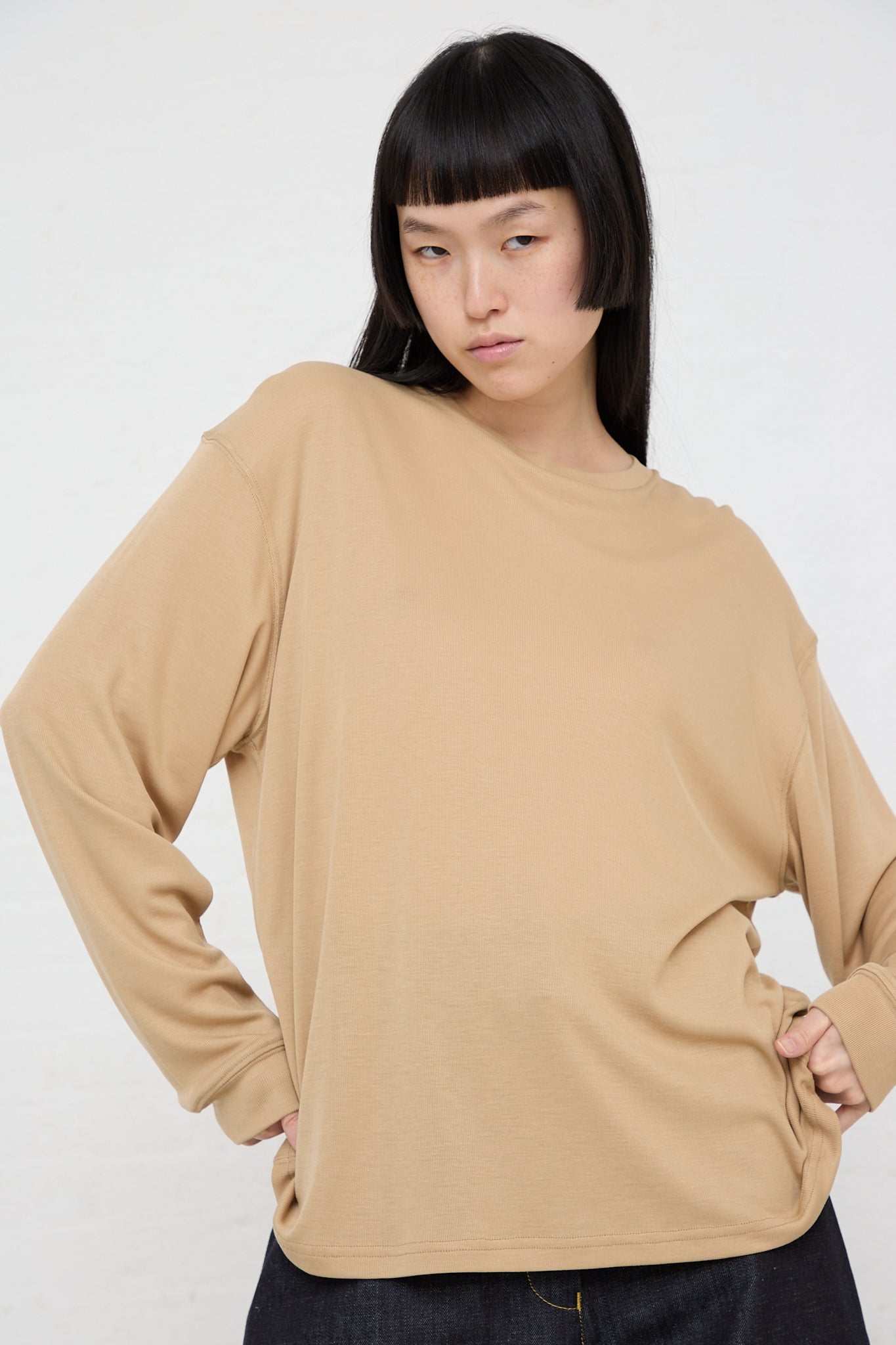 The model is wearing the Studio Nicholson Simmons Long Sleeve Top in Sand.