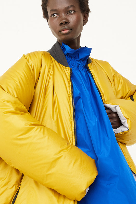 A model wearing a yellow Sofie D'Hoore Dobi Reversible Long Down Jacket and blue dress.
